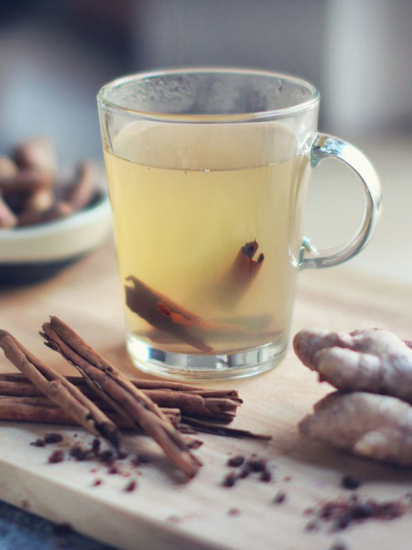 A glass of ginger and cinnamon tea on a wooden board with fresh ginger and spices
