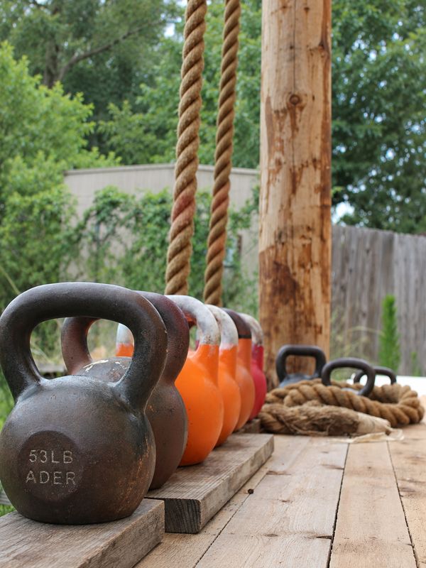 Kettlebells and climbing ropes on a wooden deck in a leafy garden