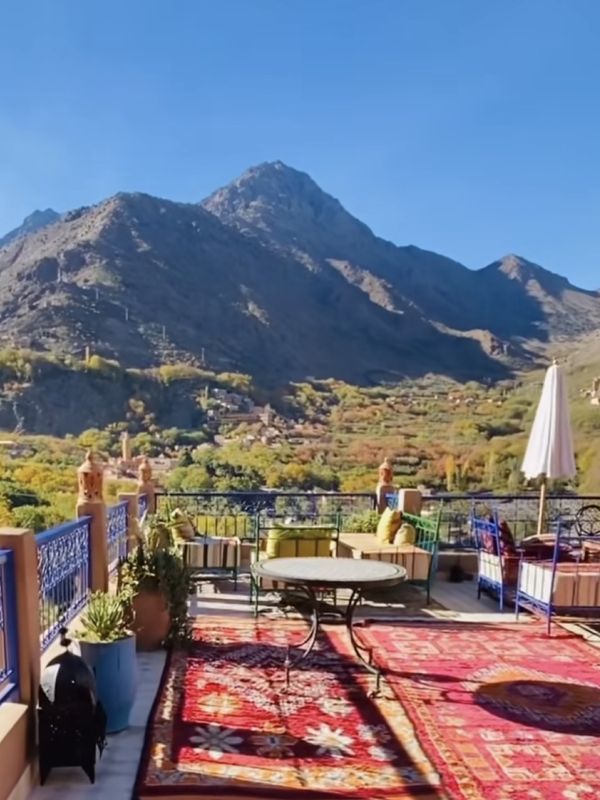 A rooftop terrace with rugs and seating facing a mountain range