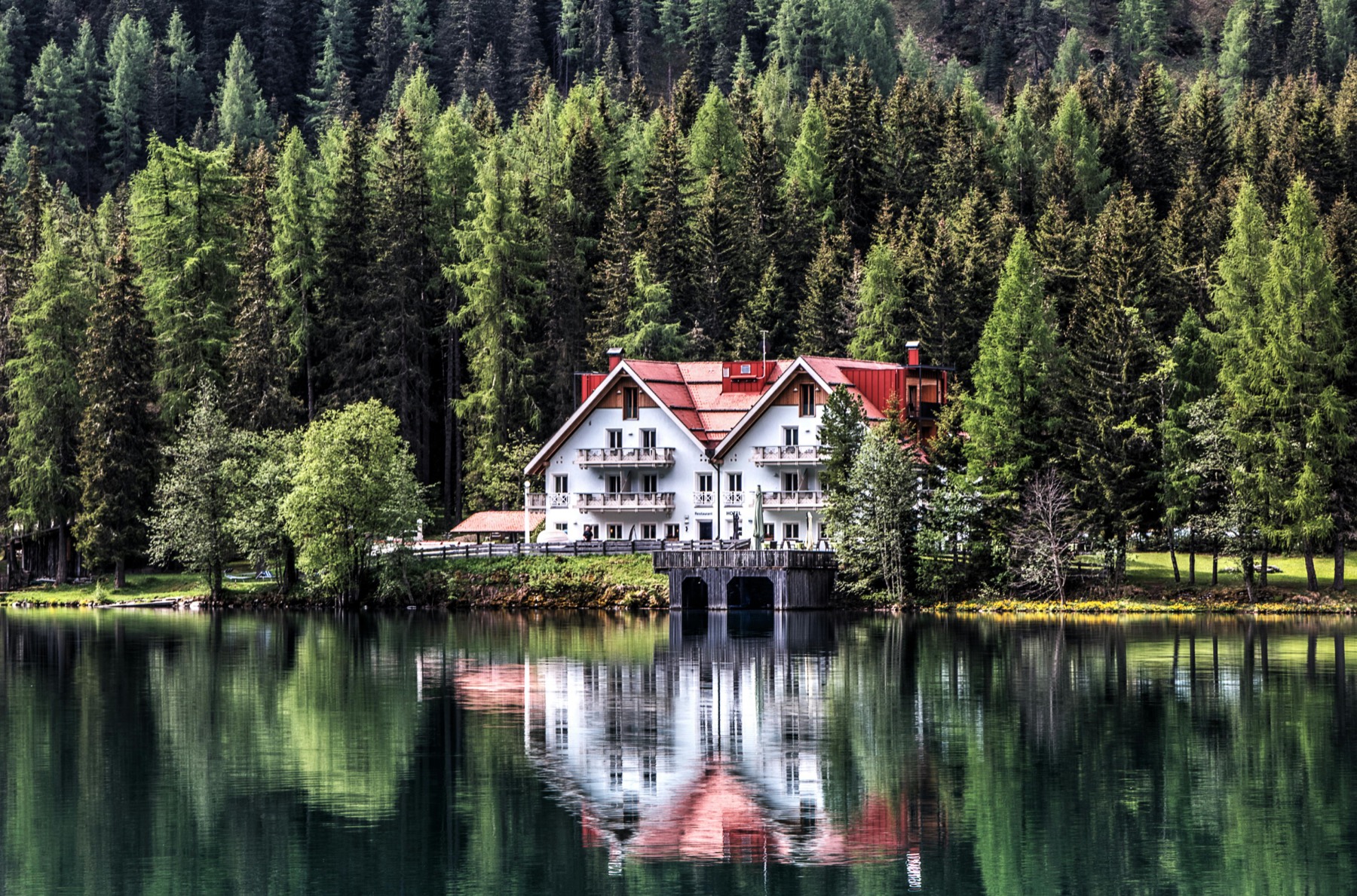 A timber lodge reflected in a still alpine lake, framed by forest